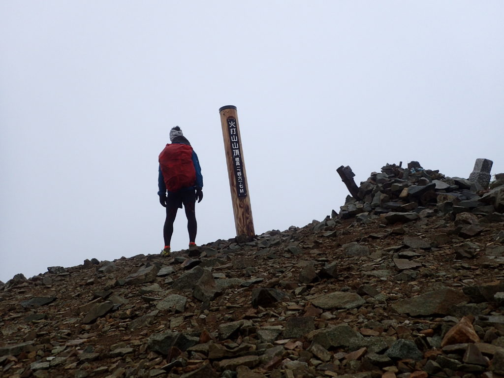 雨の火打山山頂でモンベルの登山用レインウェアであるトレントフライヤーを着て記念撮影
