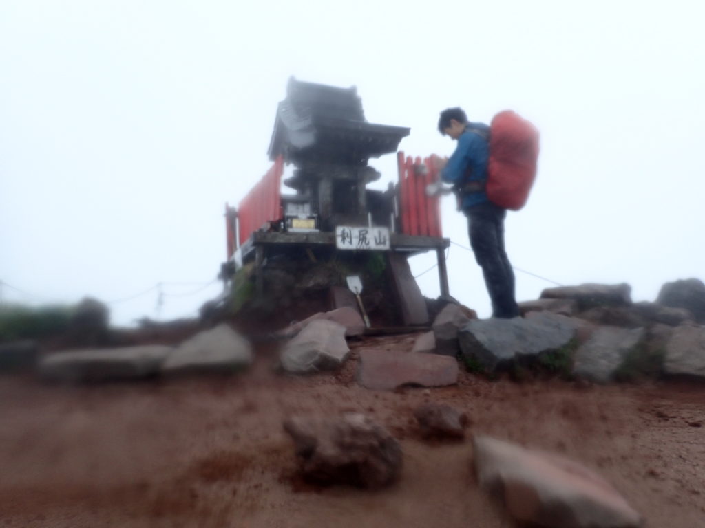 雨の降る北海道の利尻山の山頂でモンベルの登山用レインウェアであるトレントフライヤーを着て記念撮影