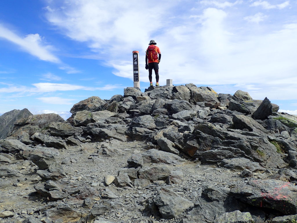 日本百名山である間ノ岳山頂に立つ背中にモンベルの登山用ザックであるバーサライトパック