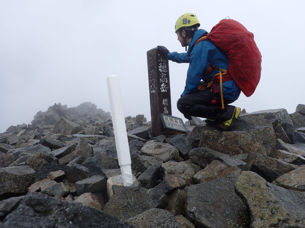 雨の前穂高岳山頂でモンベルの登山用レインウェアであるトレントフライヤーを着て記念撮影