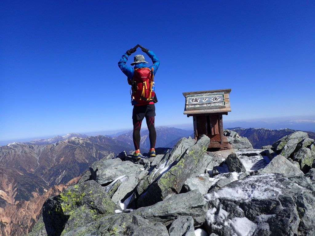 冷たい風が吹く北アルプスの槍ヶ岳山頂でモンベルの登山用レインウェアであるトレントフライヤーを着て記念撮影