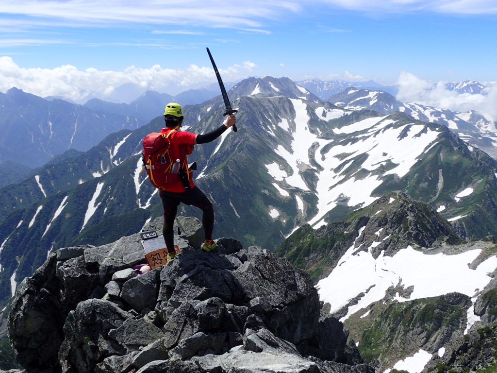 剱岳山頂で剱をかかげる背中にモンベルの登山用ザックであるバーサライトパック