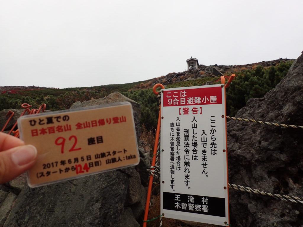 ひと夏での日本百名山全山日帰り登山で登った御嶽山の最高到達点で自作の登頂カードで記念写真
