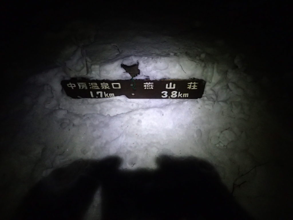 暗闇の合戦尾根で雪に埋まった道標をブラックダイヤモンドの登山用ヘッドライトであるストームの灯りで照らす。