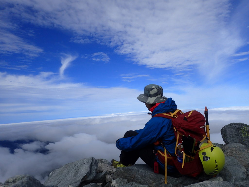 北アルプスの槍ヶ岳山頂でモンベルの登山用レインウェアであるトレントフライヤージャケットを着て記念撮影